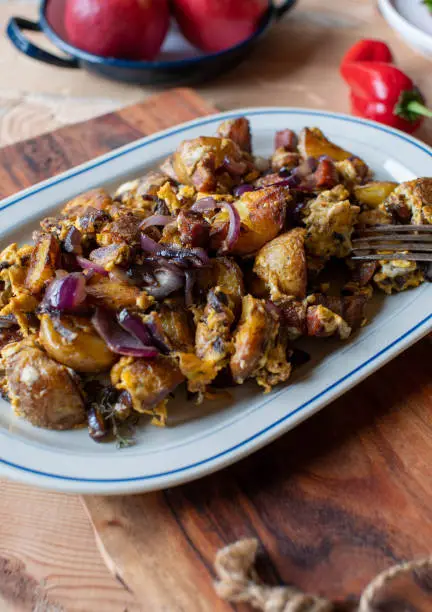 Delicious hearty meal with pan fried potatoes, scrambled eggs, chorizo sausage and red onions. Served warm and ready to eat on a plate on rustic and rural table background.