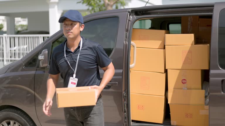 Delivery man takes out box parcel from a cargo van and goes to the house to deliver the package to the homeowner