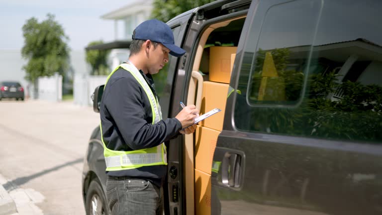 Delivery man takes out box parcel from a cargo van and goes to the house to deliver the package to the homeowner