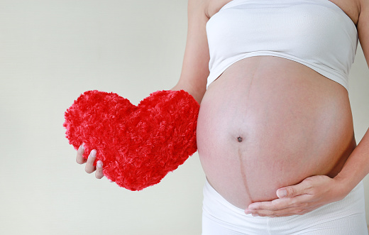 Close-up Pregnant woman holding a red heart pillow at her tummy.