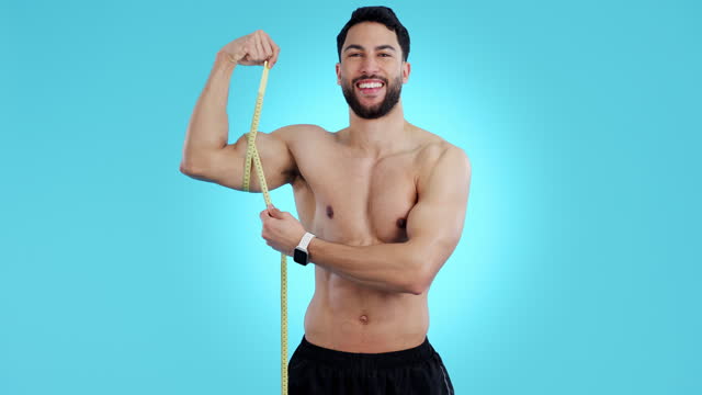 Tape measure, man and bicep arm muscle in studio for growth, development or gain. Athlete, bodybuilder or happy sports person portrait on blue background for exercise, workout and training progress