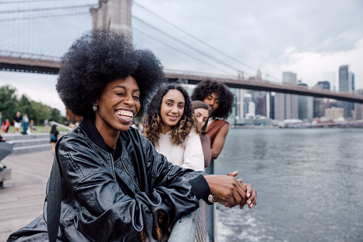 Friends portrait in the street with downtown New York skyline on the background. Group fo multi-ethnic young people posing looking at camera.