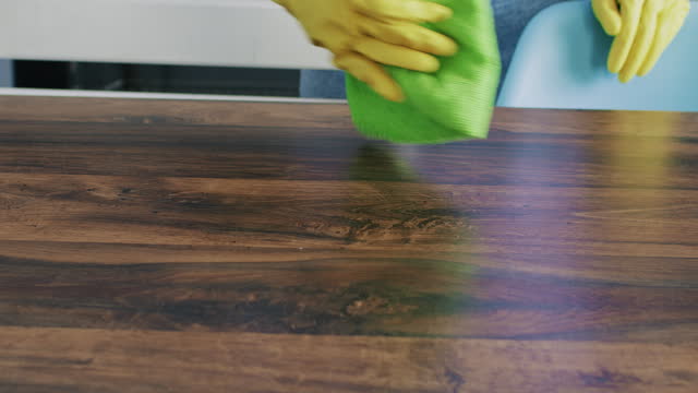 Housewife in rubber gloves wiping wooden table from dust