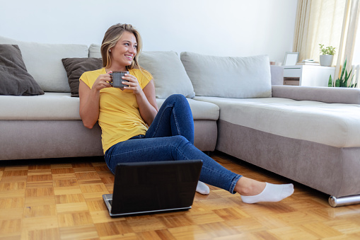 Woman, coffee and watch movies on laptop, streaming multimedia or news show on floor of home. Happy Caucasian person relax with cup of tea, computer or social media subscription of online entertainment.