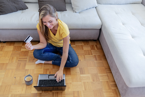 Shot of a cheerful young woman doing online shopping on her laptop while being seated on the floor at home.
