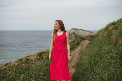 A young woman with red dress walking a path by the sea