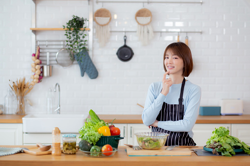 Portrait young asian woman wearing apron preparing cooking salad vegetable gesture thinking in kitchen at home, female making salad, food and nutrition, female and healthy, lifestyles concept.