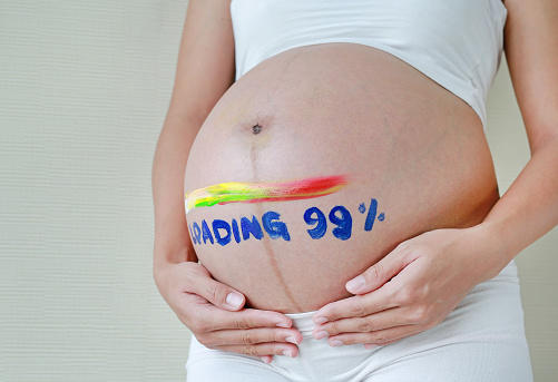 Pregnant woman holding belly with painting loading 99%. Waiting for baby concept.