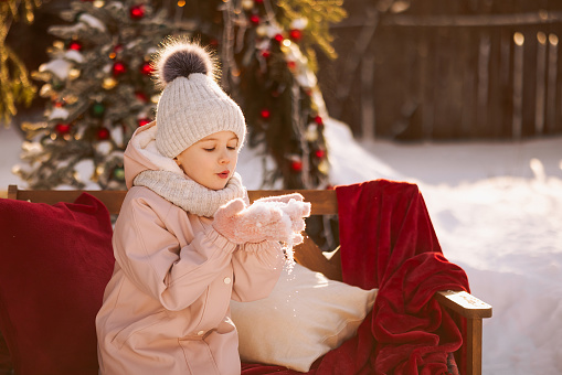 A little girl in winter clothes stands cheerfully on a decorated Christmas street in winter clothes. Christmas or New Year greetings concept.