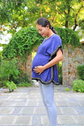 Beautiful pregnant woman touching her belly in the green garden.