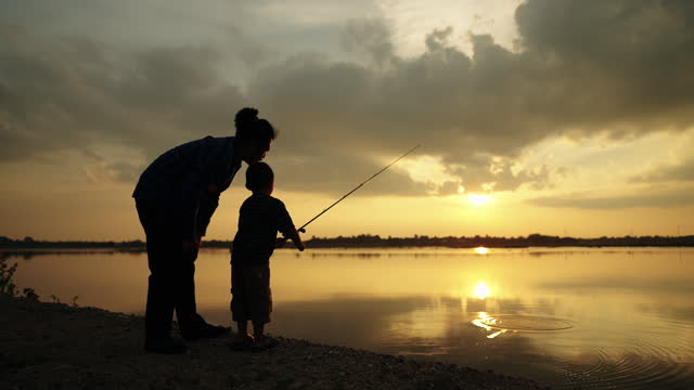 Fishermen are using fishing rods in the reservoir during Silhouette sunset, father teaching son how to fish in beautiful sunset over ocean ,activity family concept