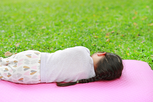 Rear view little Asian child girl sleeping on pink mattress in green grass lawn at summer park garden.