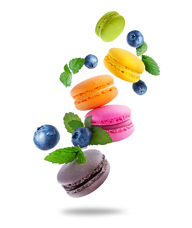 Ð¡olored macaroons with leaves of mint and blueberries. Levitating colored macaroons with different flavors isolated on a white background