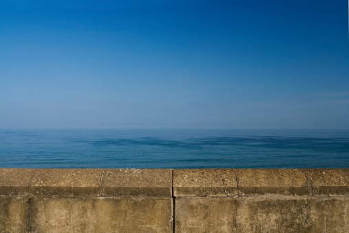 A solid concrete sea wall provides a contrast to an ethereally blue day on the coast.