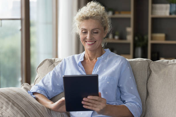 istock Happy blonde senior lady holding tablet computer at home 1744783417