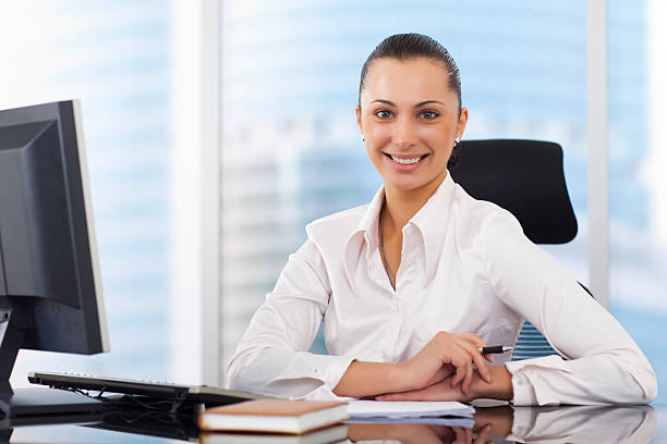 Smiling woman behind a desk with computer and notepads stock photo