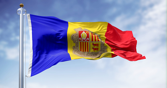 The flag of the Principality of Andorra waving in the wind on a clear day. Vertical blue-yellow-red stripes with coat of arms in center. 3d illustration render. Rippled fabric.