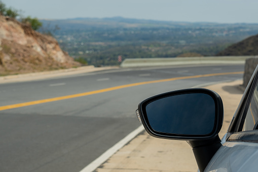 Focus on the mirror of a car, in the background you can see a mountain road.