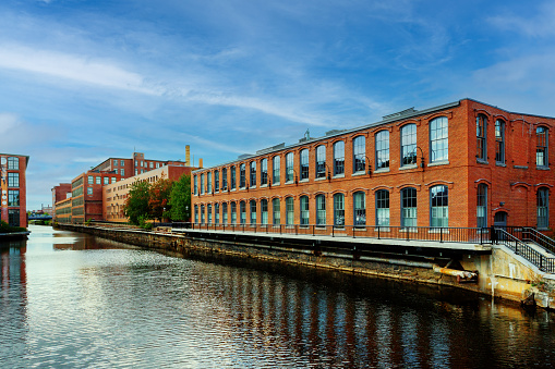 Lowell, Massachusetts, USA - October 15, 2023: Pawtucket Canal and Mill Buildings. Completed in 1796, the Pawtucket Canal was originally built as a transportation canal to circumvent the Pawtucket Falls of the Merrimack River in East Chelmsford, Massachusetts. In the early 1820s it became a major component of the Lowell power canal system. with the founding of the textile industry at what became Lowell. Incorporated in 1826 to serve as a mill town, Lowell was named after Francis Cabot Lowell, a local figure in the Industrial Revolution. The city became known as the cradle of the American Industrial Revolution because of its textile mills and factories. Many of Lowell's historic manufacturing sites were later preserved by the National Park Service to create Lowell National Historical Park.