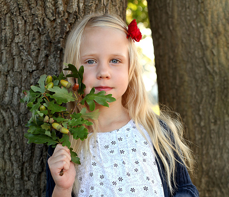 Beautiful child with green oak leaves in summer park. Happy kid girl having fun, outdoor portrait