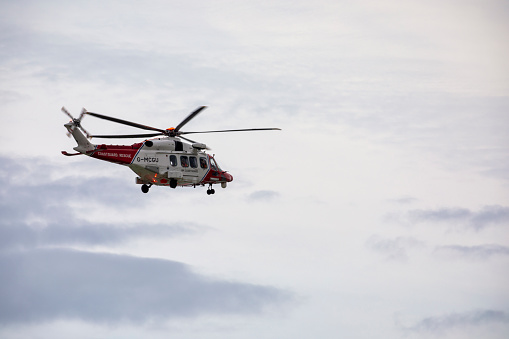 East Sussex, Beachy Head, UK 27 Jun 2020: The HM Coastguard Rescue Helicopter attending an incident on the Beachy Head cliffs flying in the sky on a bright cloudy day over the ocean.