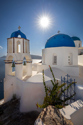 A gorgeous view of a quant church and bell tower and blue sea with sailing boat on Oia, Santorini, Greece.