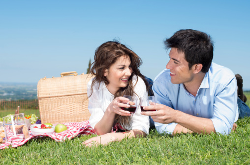 Portrait Of Happy Young Couple Lying On Grass And Enjoying Wine