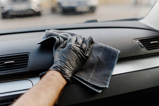 istock Man's hand in black glove cleaning car interior, dashboard and leather seats with microfiber cloth. Hand wipe down suede leather seat saloon interior. 1744855170