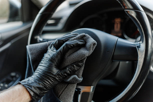 istock Man's hand in black glove cleaning car interior, dashboard and leather seats with microfiber cloth. Hand wipe down suede leather seat saloon interior. 1744855771