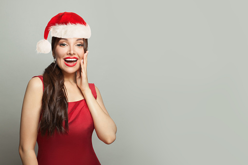 Surprised Christmas woman brunette model in Santa hat on gray background