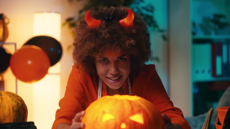 Young African American woman with devil horns showing glowing Halloween pumpkin