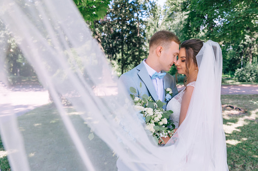 A beautiful wedding couple laughs and kisses against the backdrop of a city park.