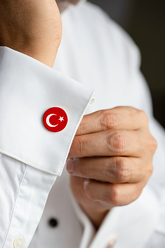 Man in white shirt wearing cufflinks. Turkish flag on cufflinks.