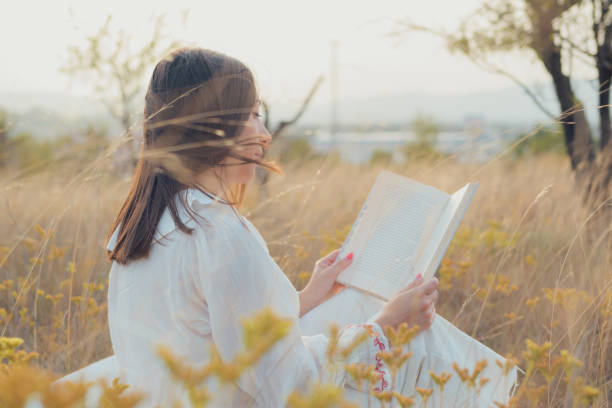 istock Woman with a book reading on a meadow at sunset 1744957653