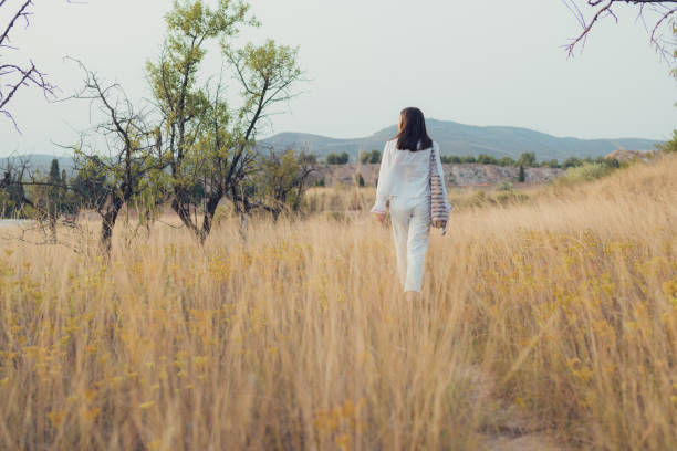 istock Young woman dressed in white walks through a meadow at sunset 1744957670