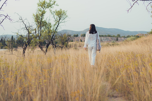 Young woman dressed in white walks through a meadow at sunset