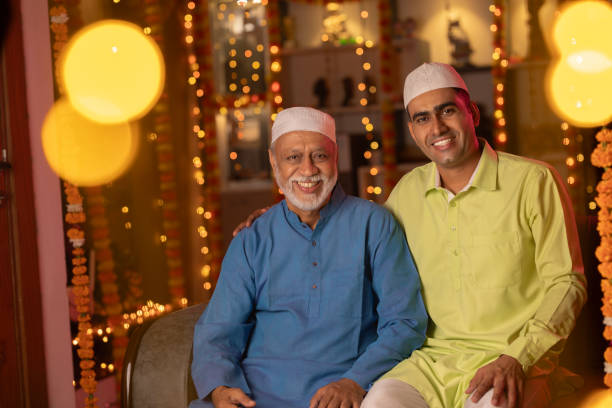 istock Father and son in kurta and skull caps sitting at illuminated home 1744986483
