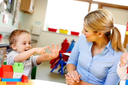 Cute little kid with teacher playing in play room at preschool