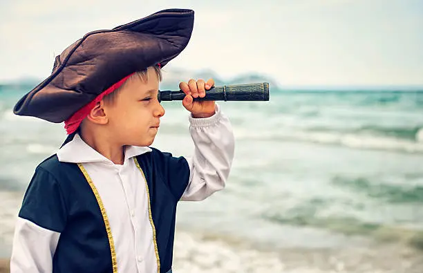 Little boy dressed up as pirate looking through spyglass.