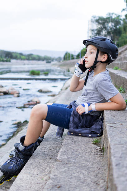 istock Cute boy is preparing for roller skating near the river. He is talking on his mobile phone while he is waiting for his friends. 1744997626