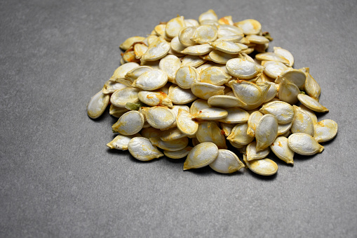 Heap of fresh and organic pumpkin seeds on gray stone texture with copy space