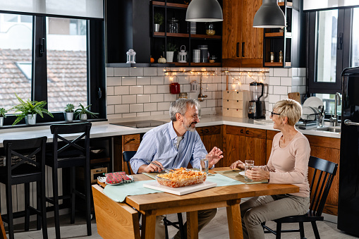 A cheerful mature couple talking while eating a delicious homemade lunch. They are ready to have a great time together while eating. Sunday routine.