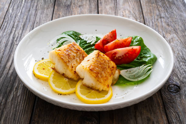 istock Fried cod fillet and fresh vegetables on wooden table 1745024352