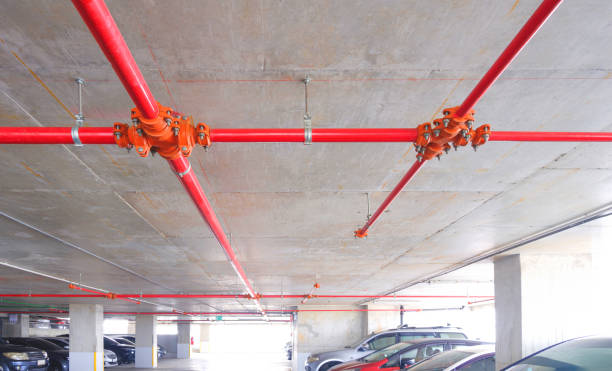 istock Red fire protective water pipeline system on concrete ceiling with many vehicle parked inside of parking garage building 1745027174