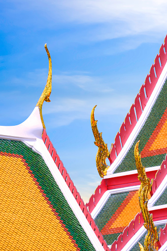 Beautiful gabel apex with ornamental roof point and colorful ceramic tiles roofs of the Emerald Buddha temple in Wat Phra Kaew at Grand Palace against blue sky in vertical frame