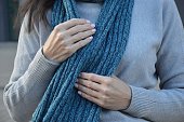A woman in a gray sweater holds a warm knitted scarf with her hands. Woman's hands hold a turquoise scarf. Close-up.