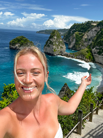 Young female tourist taking selfie at the  Manta Bay or Kelingking Beach on Nusa Penida Island, Bali, Indonesia