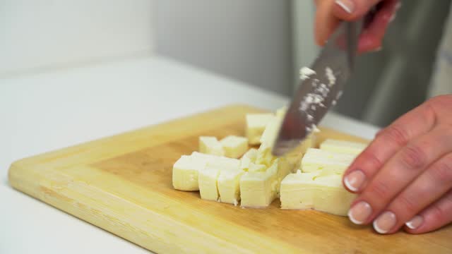 A woman cuts feta cheese on a kitchen board.