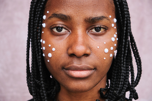 Frontal view of afro woman looking at camera with adhesive pearls on her face.