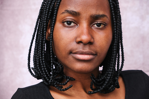 Portrait of afro woman with faux locs braids looking at camera with her black eyes with a background behind.